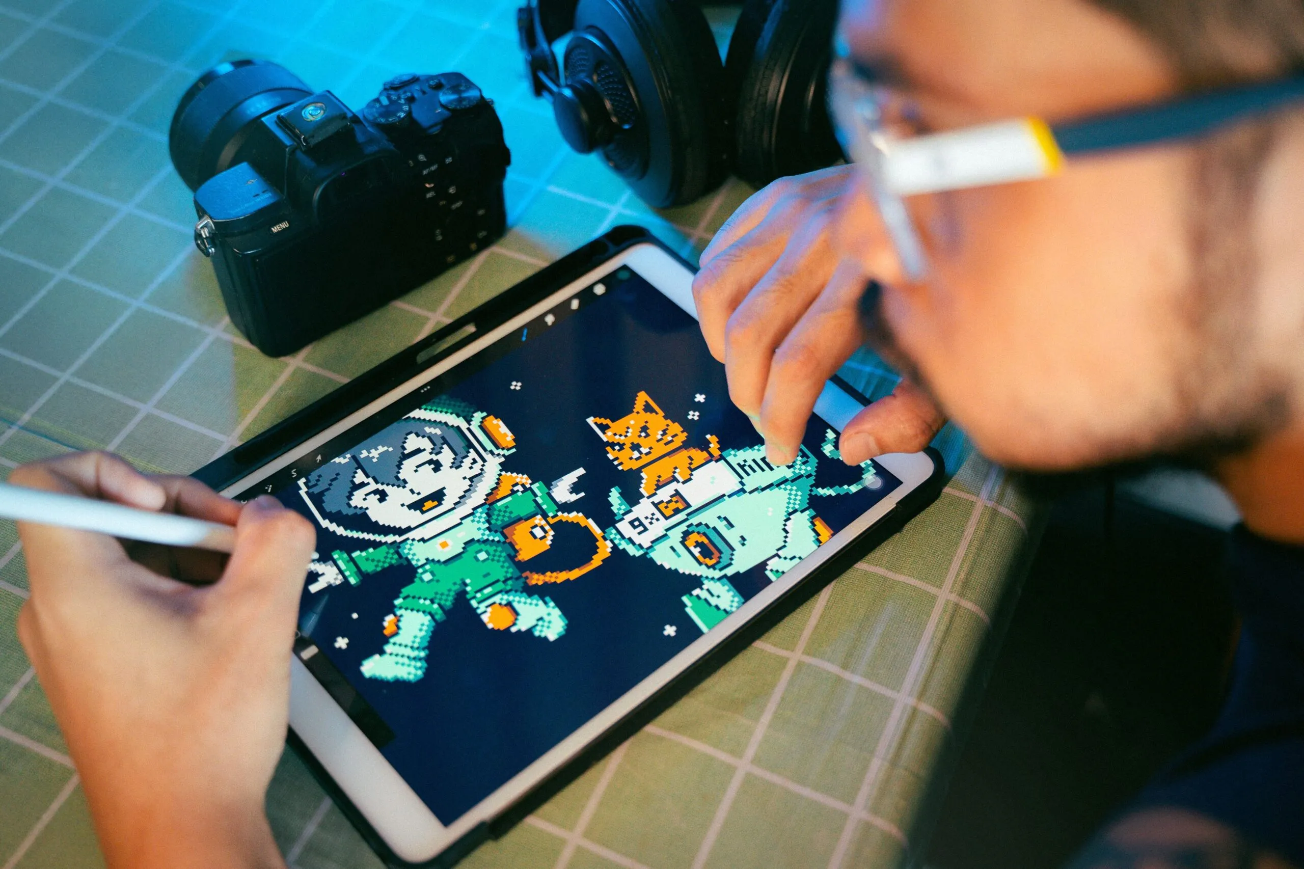 Person drawing digital art on a tablet using a stylus next to camera and headphones.